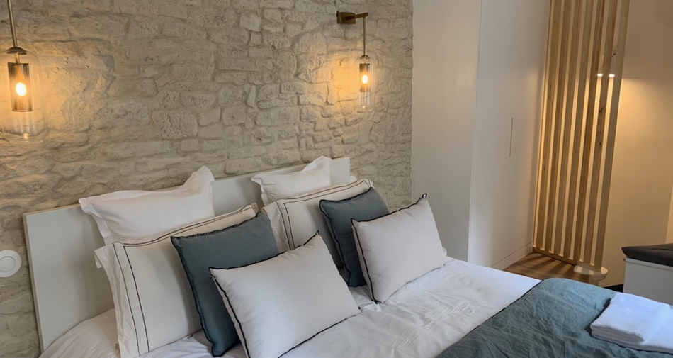 Valoriser Murs Intérieurs Maison avec chambre équipée d’un parement en pierre reconstituée derrière une tête de lit en bois.