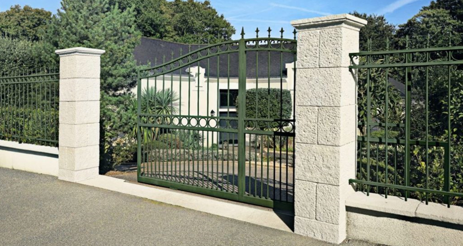 Piliers portail pierre élégants en pierre reconstituée ORSOL encadrant un portail en fer forgé à l’entrée d’une propriété résidentielle
