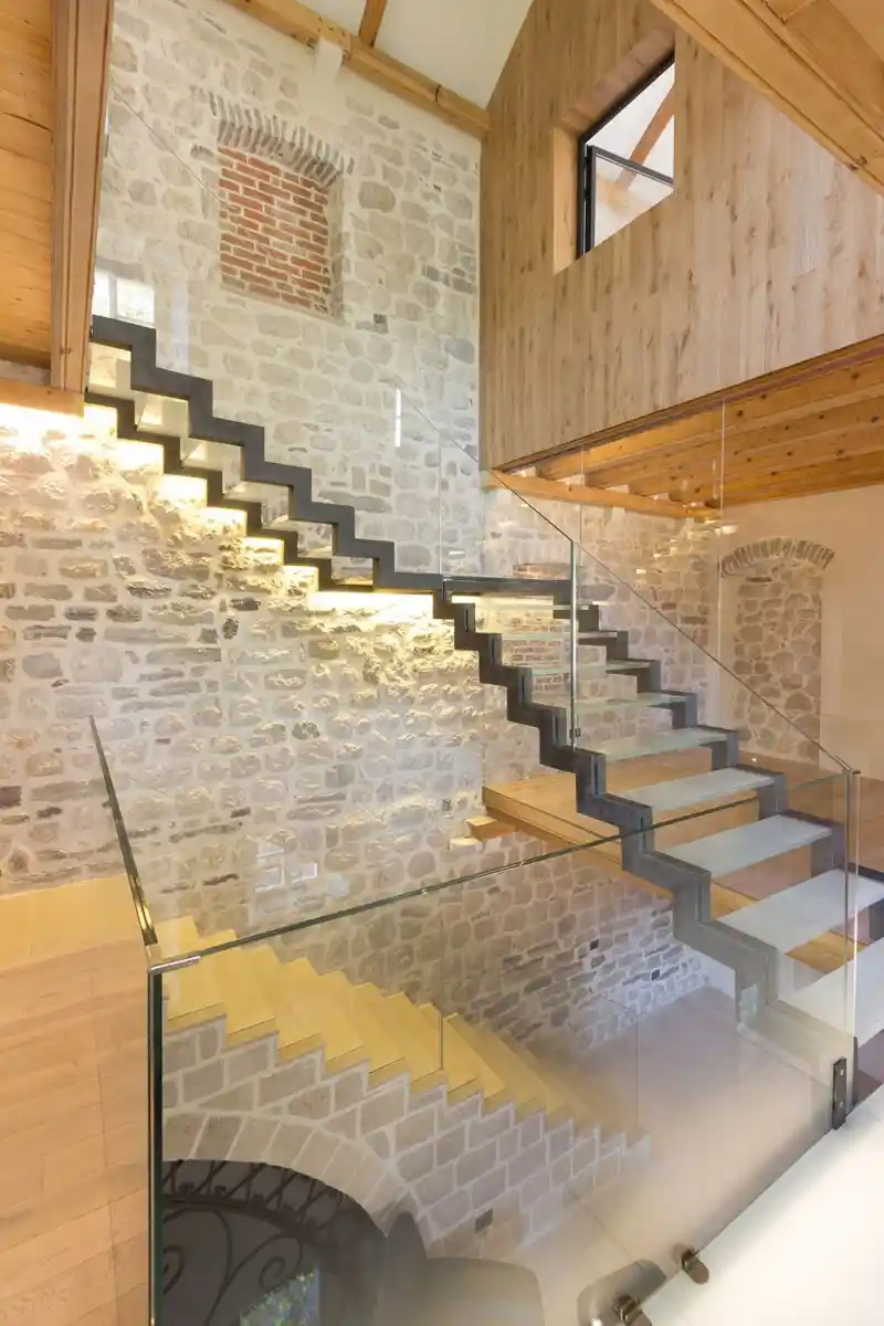 Escalier moderne en verre et bois avec mur en pierre reconstituée et plaquette de brique, illustrant notre expertise en matériaux nobles chez Orpa Matériaux (Elaustore).